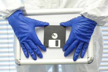 two hands in blue gloves presenting solution - program on old school diskette