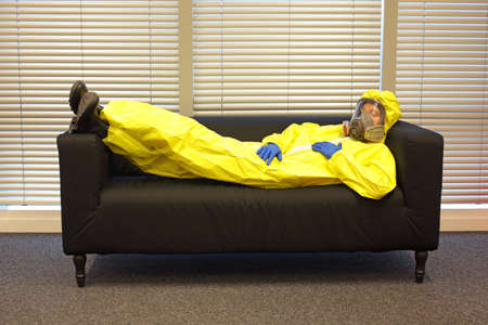 professional in protective clothing, mask and gloves, lying and relaxing on the couch in officeの写真素材