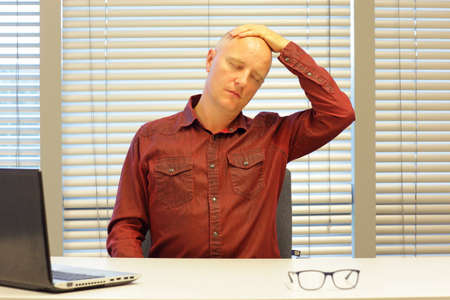 middle age balding man relaxing neck - short break for exercise on chair in officeの写真素材