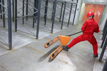 Young worker in uniform exercising with pallet truck in warehouse