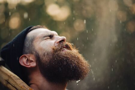Brutal brunette bearded man in warm hat with a hatchet in the woods on a background of treesの写真素材