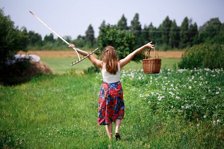 Girl in a bright skirt and wicker basket walks in a green fieldの写真素材