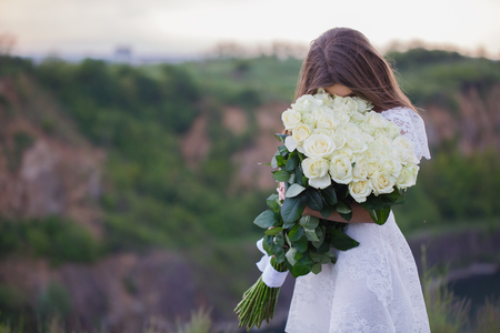 happy girl in a white dress holding a large bouquet of white rosesの写真素材