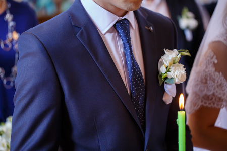 The groom in a blue suit and tie holding a white candle in churchの写真素材