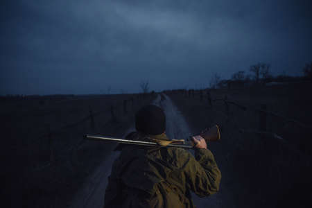 Old bearded man hunter in a warm hat, in a khaki jacket with a hunting rifle and a large backpack...