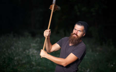 a man lumberjack with a long curly beard in a warm hat and a dark T-shirt with an iron ax on his...