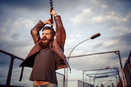 Mad rock guitarist with gray hair and a big beard with a mustache in a brown leather jacket and blue...