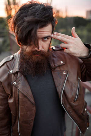 Mad rock guitarist with gray hair and a big beard with a mustache in a brown leather jacket