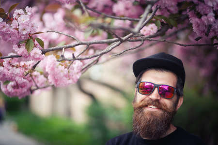 Cheerful bearded male developer with a long beard and dark gray hair in a shirt and jeans hugs a...