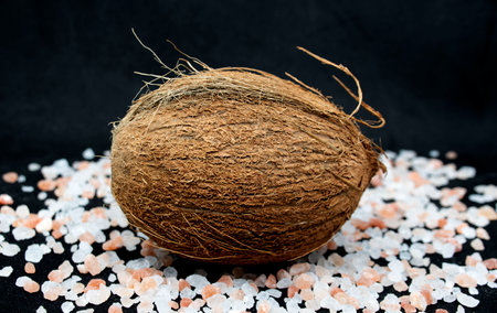 Coconut with pink sea salt on black background.