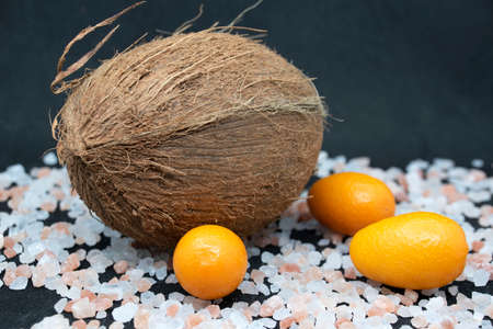 Coconut and kumquat with pink sea salt on black background.の写真素材