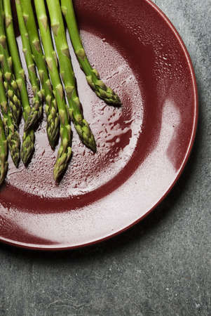 Some asparagus over red dish with water dropsの写真素材