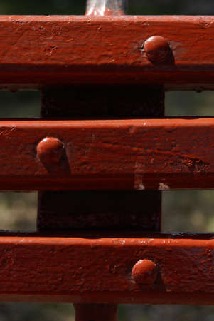 close up and  detail of endorsement of wood seat painted of red color and three metallic rivets painted of red color  all illuminating of lateral form by the light of the sun の写真素材