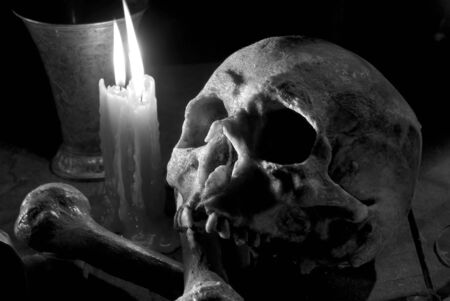 real skull and bones over a table, with candles and chalice.