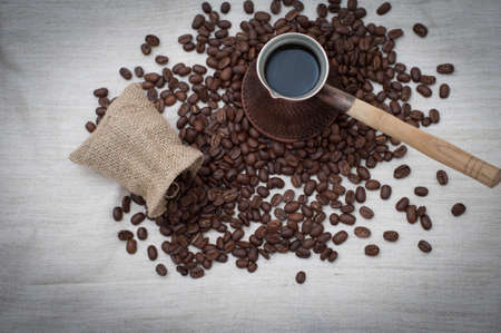 Bean coffee and turkish pot. Turks and grains are scattered on burlap backgroundの写真素材
