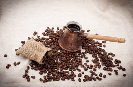 Bean coffee and turkish pot. Turks and grains are scattered on burlap backgroundの写真素材