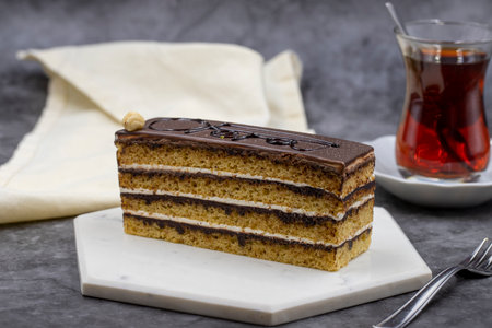Opera cake on dark background. Cake with cream and chocolate filling. along with a cup of tea