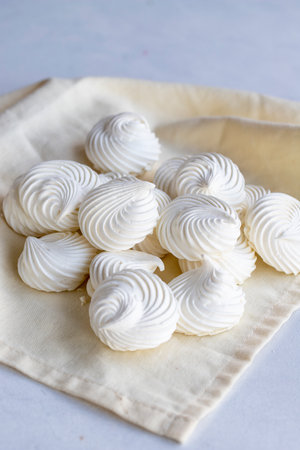 Small white meringues on white fabric. macro shot. vertical view