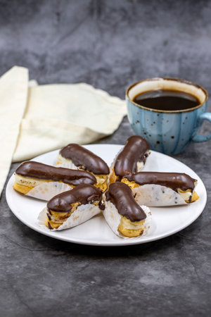 Tasty eclairs and cup of coffee on dark table. Traditional french dessert. Pastry products. close up