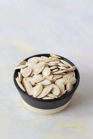 Pile of pumpkin seeds in bowl on white wooden backgroundの写真素材