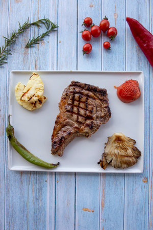 Beef steak on blue wooden background - with roasted tomatoes, onions and peppersの写真素材