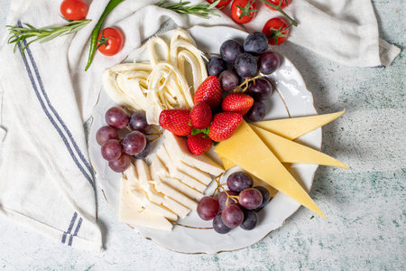 Cold cheese plate, cheese set plate. Strawberry, grape and cheese assortment on gray background. Top...