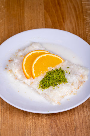 GÃ¼llaÃ§ dessert on wood background. Traditional Ramadan dessert. GÃ¼llaÃ§ dessert topped with orange slice and pistachio. close upの写真素材