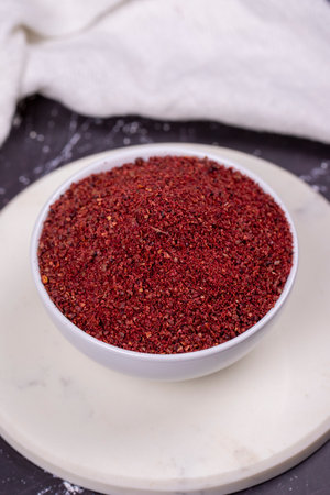 Sumac on dark background. Dried ground red Sumac powder spices in wooden bowl. close up