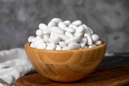 Almond Candy. Sugar coated almond candy in wooden bowl on dark background. Small multi-colored...