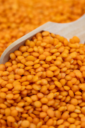 Red lentils on wooden spoon. Legumes as background. close-up raw red lentils
