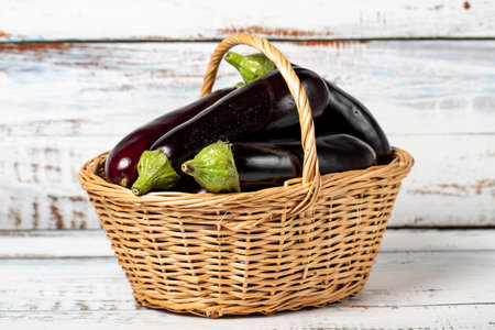 Fresh raw eggplant in a basket over wooden background. Eggplant harvest season concept. Vegetables for a healthy dietの写真素材