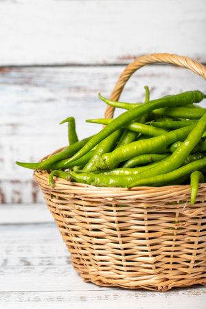 Fresh green pepper in a wicker basket over wooden background. Green chili pepper harvest season concept. Vegetables for a healthy diet. close upの写真素材