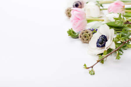 Pink tulips, white anemones, pink cloves and white buttercups with green leaves lying on white background on the right top side of the pictureの写真素材