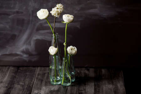 Four white buttercups and blossom apple in small, glass bottles standing in the dark wooden floor...