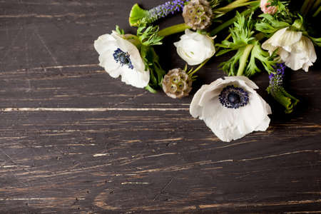 White anemones and white buttercups lying on old, dark wood in the right topの写真素材