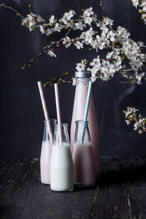 Three small bottles of strawberry milkshake and milk with straws with one big bottle standing on dark backgroundの写真素材