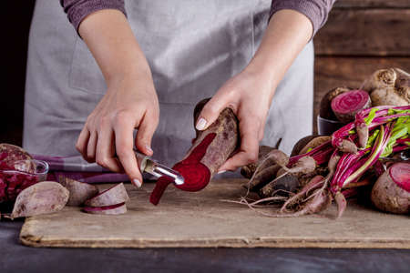 ook in gray apron is peeling a beetroot with vegetable peelerの写真素材