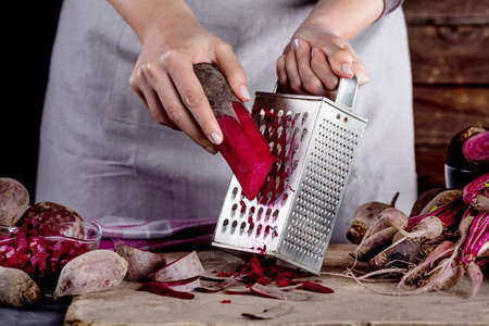 Cook in gray apron is grating a beetroot with vegetable rasperの写真素材