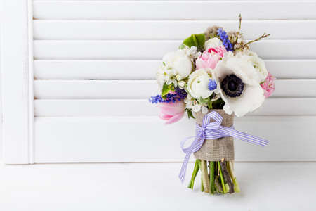 Bouquet from pink tulips, violet grape hyacinths, white anemones, violet veronica and white buttercup with violet ribbon with white wooden shutter backgroundの写真素材