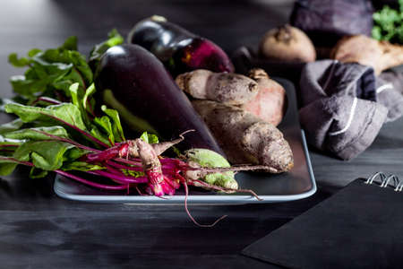 Beetroots, aubergines and beet leaves on the plate with black notebook on the sideの写真素材