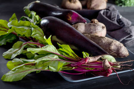 Beetroots, aubergines and beet leaves on the plate with dark clothの写真素材
