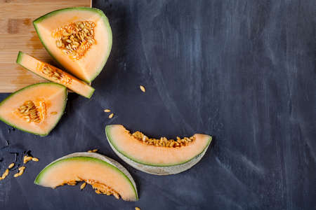 Slices of melon on cutting board on black board