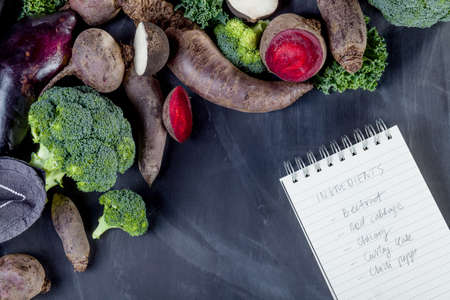 Beetroots, curly kale, broccoli and black turnip with cloth lying on blackboard with notebookの写真素材