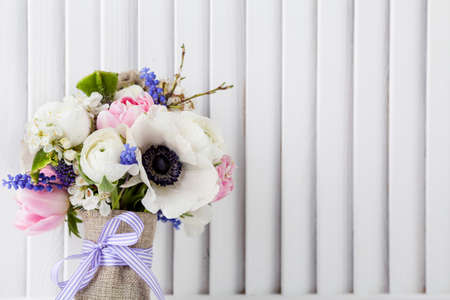 Pastel bouquet from pink tulips, violet grape hyacinths, white anemones, violet veronica and white buttercup with violet ribbon with white wooden shutter backgroundの写真素材