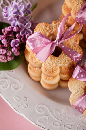 Cookies with pink ribbons on a white plate with lilac flowersの写真素材