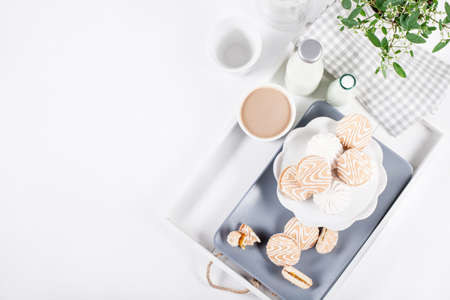 Cookies on white and gray plate with cups of coffee and bottles of milk on white shutters background with green and white flower, top viewの写真素材