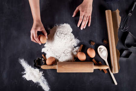 Ingredients like eggs, flour, cinnamon, anise, rolling pin, paper on blackboardの写真素材