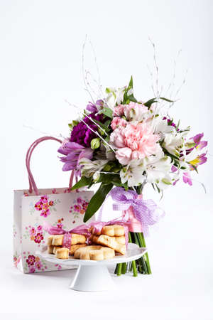 Pastel bouquet from pink and purple gillyflowers and alstroemeria on white background with gift and cookiesの写真素材