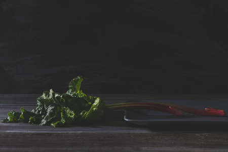Organic pieplant lying on gray plate and old wooden table with blackboard in backgroundの写真素材