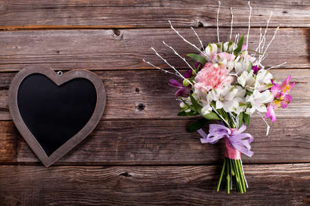 Rustic bouquet from gillyflowers and white alstroemeria on old, rustic wooden background with wooden heartの写真素材